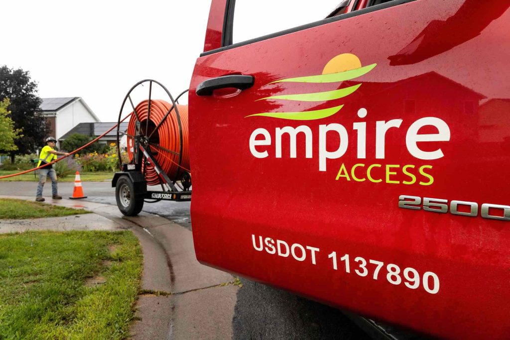 Side door view of an Empire Access truck, employee, and equipment in the neighborhood